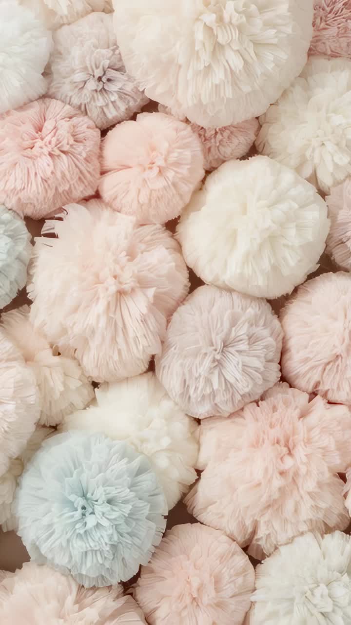 Vertical video: Panning camera shifting across pastel yarn pom-poms on studio table, showing fibers