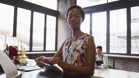 Portrait-of-happy-african-american-woman-working-at-a-cafe-bar,-holding-open-sign-and-smiling