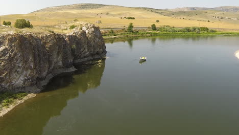 Drone-shot-Missouri-River-along-rocky-cliff,-people-fishing-in-rowboat