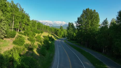 scenic driving route with asphalt road and bike lane between lush vegetation on summer blue sky background in anchorage, alaska