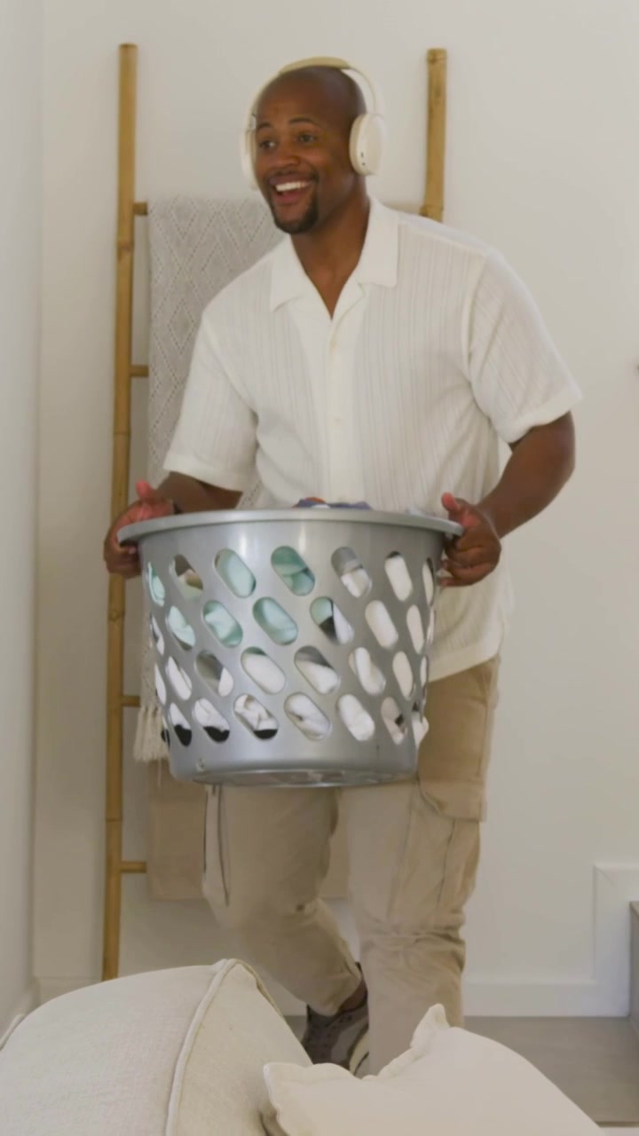 Vertical video: Hearing music, man wearing headset carrying basket down steps into kitchen, sorting
