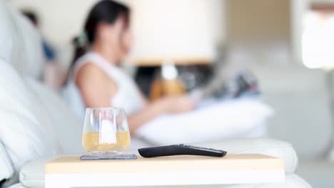 a woman sits on a modern sofa in a bright living room, reading a magazine. a remote control and drink rest on a nearby table. shallow depth of field, static camera