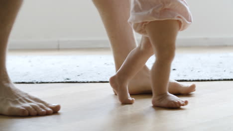 Bebé-Descalzo-Aprendiendo-A-Caminar-Con-La-Ayuda-Del-Padre.