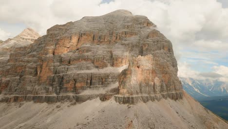 FPV-drone-races-towards-and-ascends-the-massive-Col-De-Bos-mountain-in-the-Italian-Dolomites,-surrounded-by-partially-cloudy-summer-skies