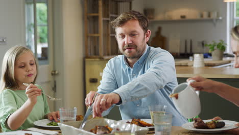 parents serving food as family sit around table at home enjoy meal together