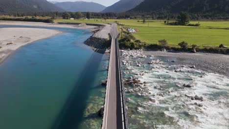 Einspurige-Brücke,-Die-Die-Ufer-Des-Wunderschönen-Blauen-Flusses-In-Bergiger-Landschaft-Verbindet