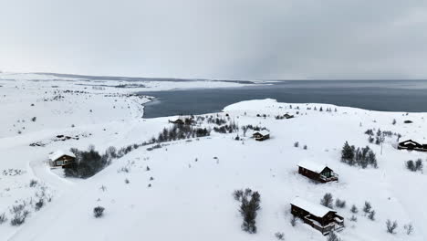 Wooden-holiday-chalets-in-a-wintry-landscape-with-a-beautiful-view-of-the-sea-on-a-cloudy-day