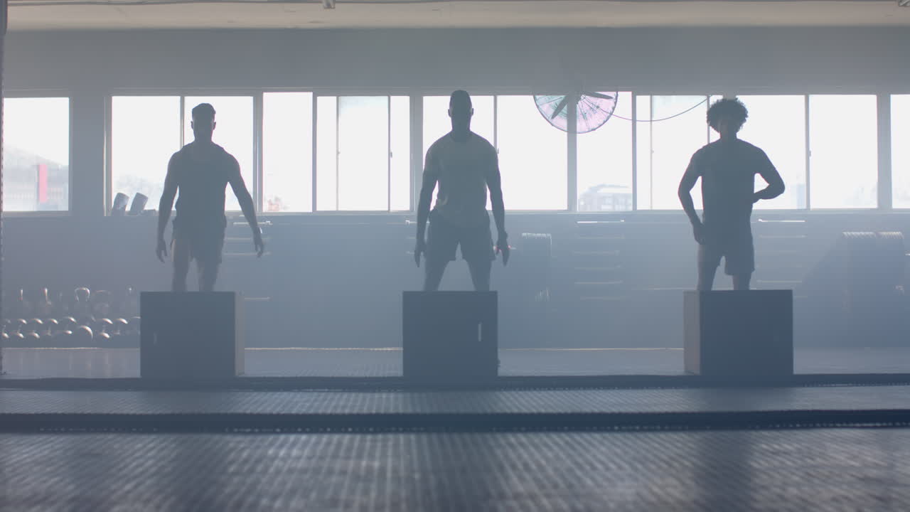 Exercising in gym, three men doing box jumps, focusing on fitness training
