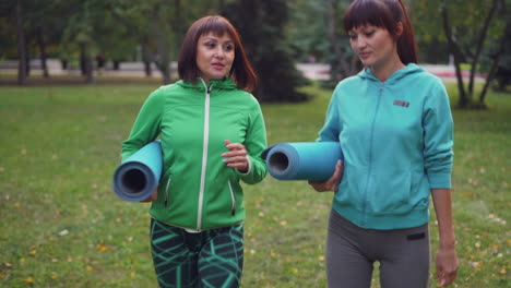 two women walking in a park with yoga mats