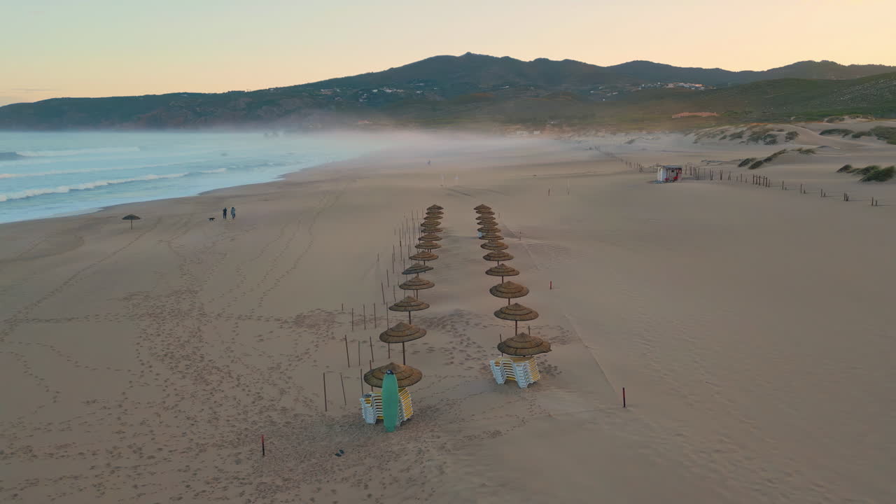 Sunset beach straw umbrellas drone panorama. Beige sandy surface with footprints