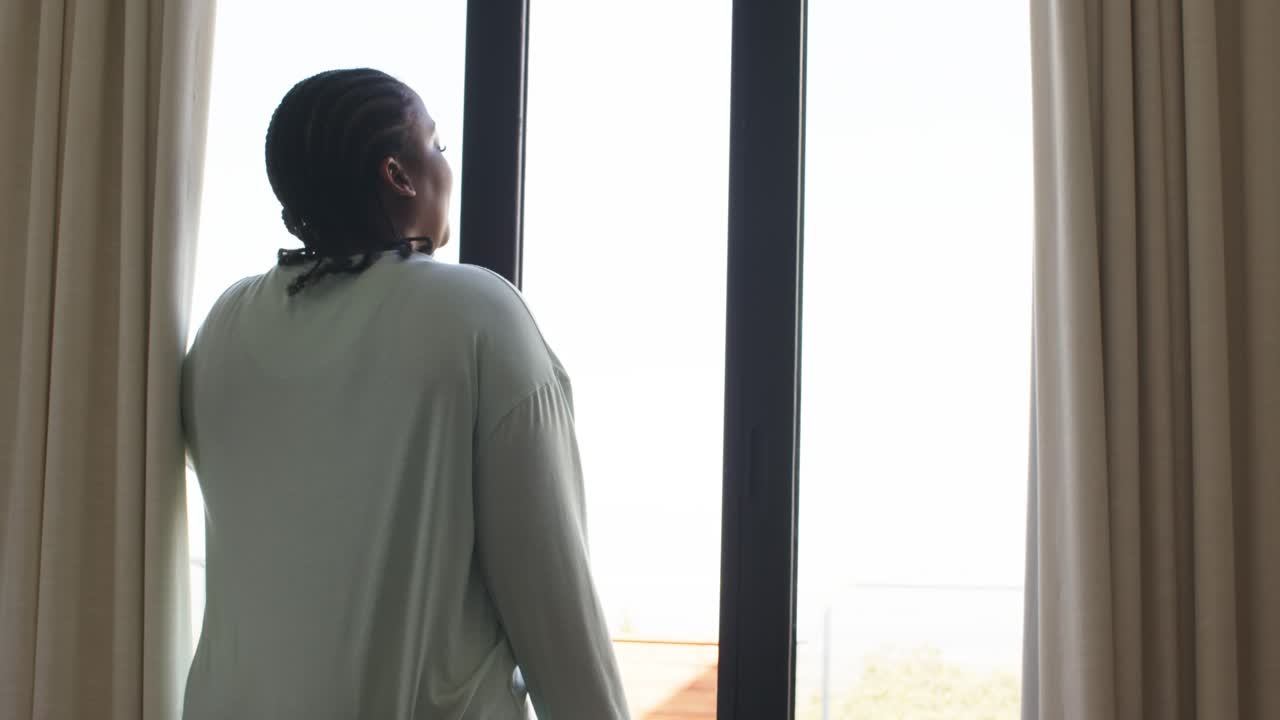 Donna afroamericana a casa che apre una porta scorrevole e le tende che rivelano un balcone