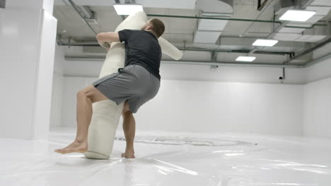 a strong mma fighter is training to throw a scarecrow. testing wrestling equipment.