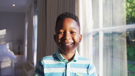 portrait of happy african american boy looking out of sunny window, turning to camera and smiling