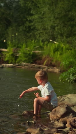 little boy entertains on riverside throwing stone into lake during summer season. cute toddler child spends time enjoying fantastic view of reservoir on sunny day