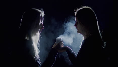 a woman and a teenage girl sit side by side and look at a candle burning in the dark