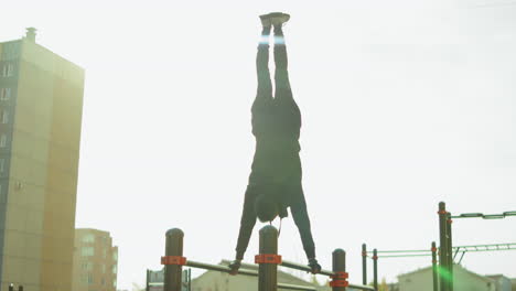 sportsman doing handstand on parallel bars at workout playground