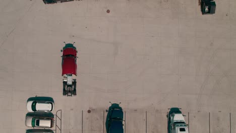 top down aerial of a red semi bobtail backing up to a reefer - dry van trailer to hook it up while another truck driver passing in front