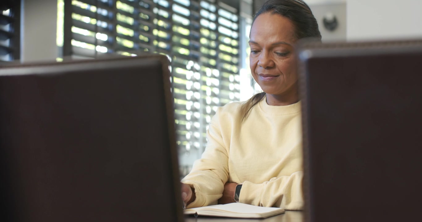 African American mature woman lifting pen and writing in notebook at wooden table, studying notes