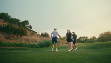 Golf foursome celebrates with a high five on the par 3 tee box after a male golfer hits a clean iron shot. Warm golden hour light highlights the group’s excitement and camaraderie on the course.