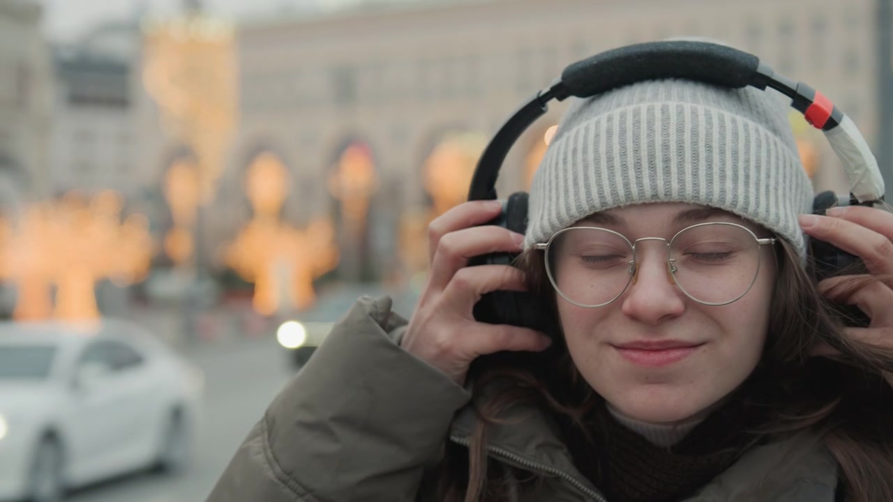 Momento di quiete in città. Donna che ascolta pacificamente in mezzo al traffico. Signora serena si gode la musica vicino a luci trafficate. Donna tranquilla con gli occhiali assorbe la musica vicino a semafori affollati al crepuscolo.