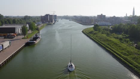 aerial shot of a sailboat sailing on the canal through walcheren towards the historical town of middelburg in zeeland, the netherlands, on a warm, sunny summer evening