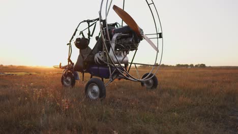 el parapente de motor se encuentra en el aeropuerto en los rayos de la luz del atardecer. en el fondo, el avión despega. la cámara se mueve a lo largo de la órbita
