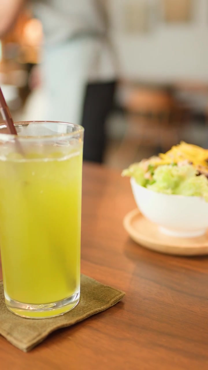 Camarero coloca té verde y ensalada en mesa de madera en cafetería luminosa, informal y con luz natural