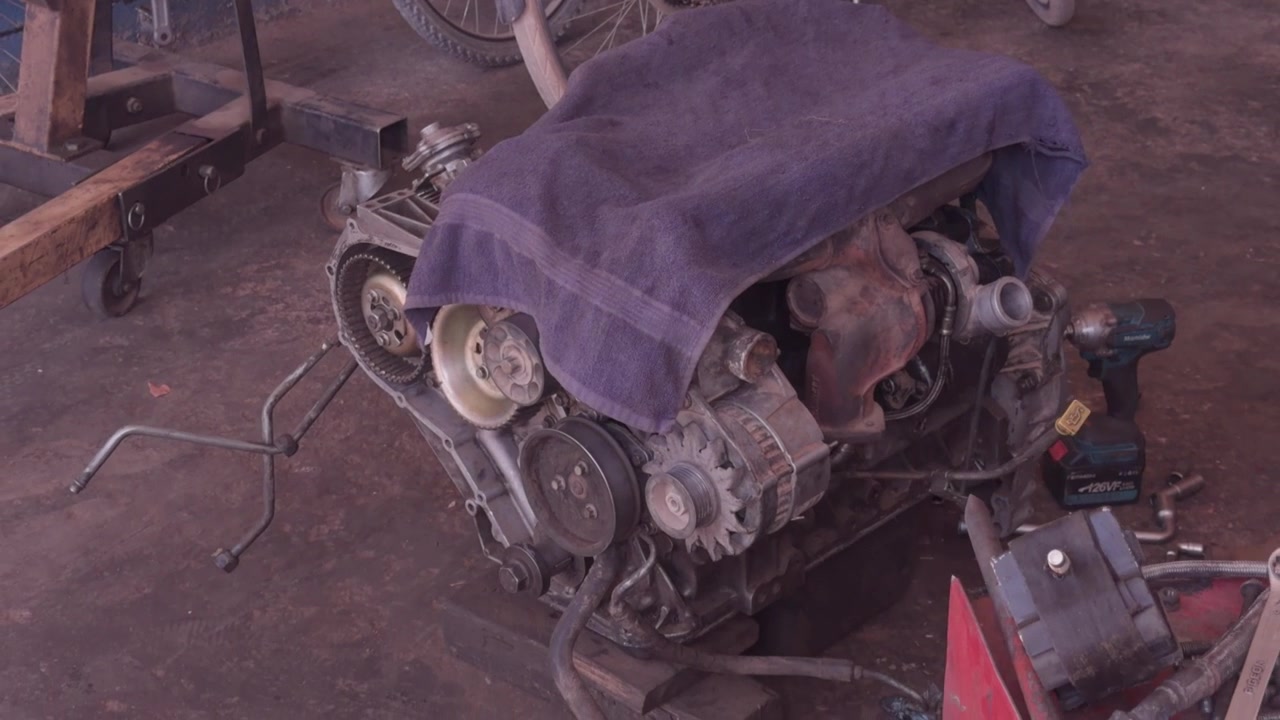 Old disassembled car engine covered with grey cloth on concrete garage floor beside a bicycle wheel