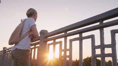 A-Woman-Stands-At-The-Railing-Of-The-Bridge-Looking-Into-The-Distance