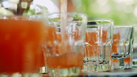 Pouring-orange-shots-in-small-glasses-through-sieve,-close-up