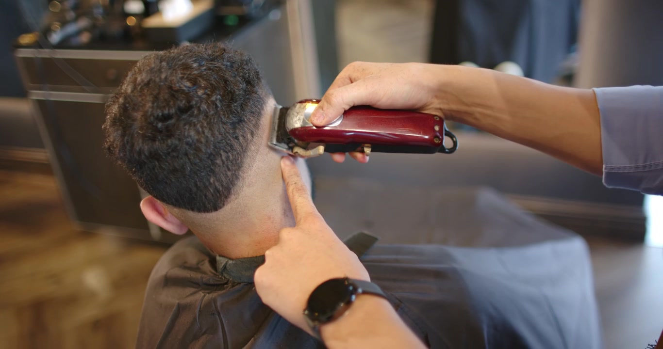 Mandlig barber og kunde, hvor barberen fører rød klipper til nakken, trimmer og forfiner fade-frisure i butikken.