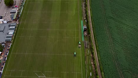 Toma-Aérea-Lenta-De-Dos-Tractores-Cortando-El-Césped-En-El-Campo-De-Rugby-De-Canterbury-En-Kent