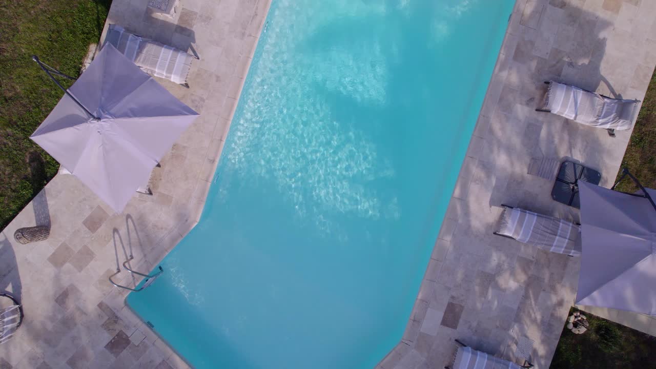 En swimmingpool set fra himlen, en optagelse der roterer, mens den stiger op i luften, med åbne parasoller og liggestole