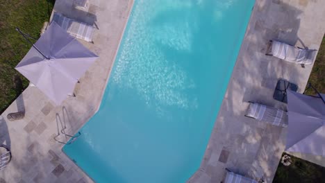 a swimming pool seen from the sky, a plan which rotates while rising in the air, there are open parasols and deckchairs