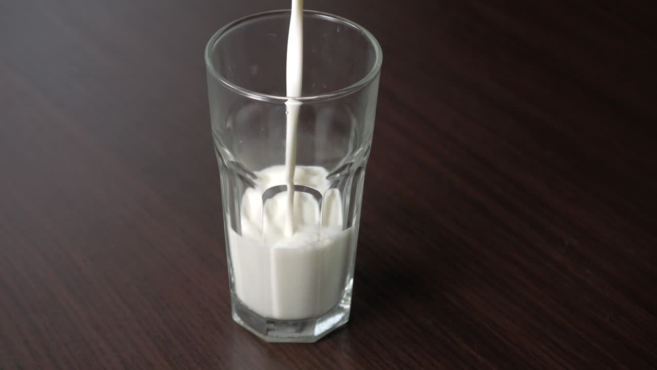 verter leche de vaca en un vaso alto sobre una mesa de madera