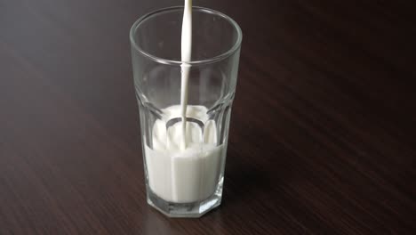 pouring cow milk into a tall glass on a wooden table