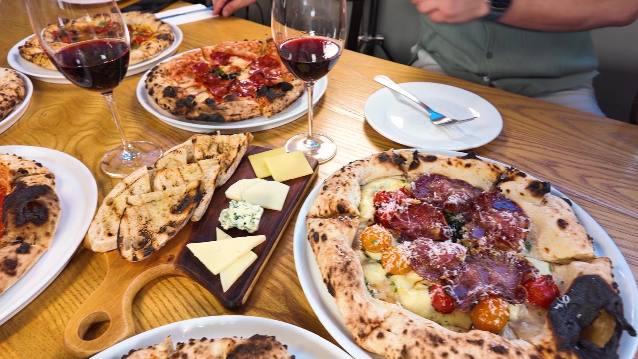 Inquadratura dall'alto di una persona che taglia pizza napoletana fresca su un tavolo di legno di un ristorante.
