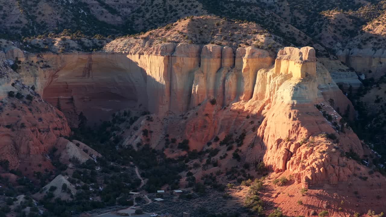 En filmisk luftoptagelse fanger det varme solnedgangslys, der fokuserer på en massiv sandstensklippeformation ved siden af et naturligt amfiteater. Denne robuste ørkenudsigt er ideel til eksklusive rejsedokumentarer
