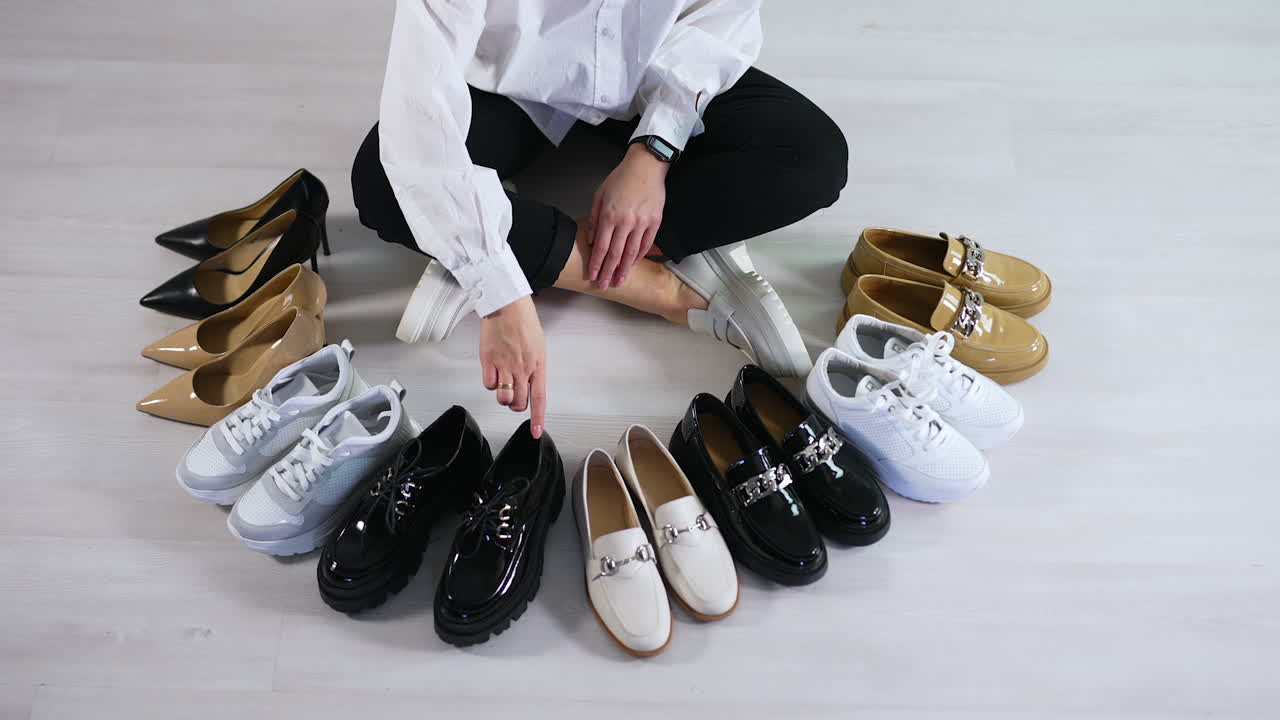 Woman sits on the floor with displayed footwear in front of her. Lady counts the shoes of diverse colors and types. Top view.