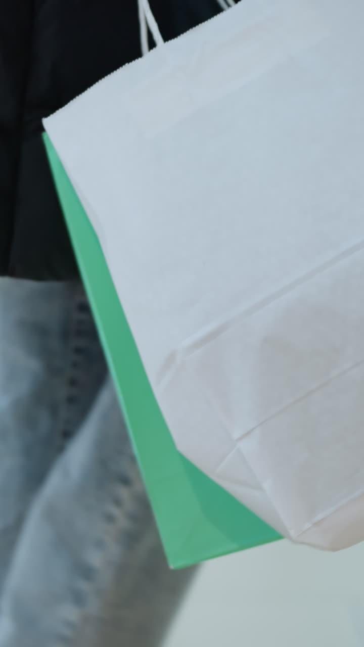 vista lateral de una persona caminando por el espacio minorista en un centro comercial bien iluminado llevando grandes bolsas de compras, maniquín vestido con ropa y prendas de vestir dispuestas en estantes visibles en el fondo