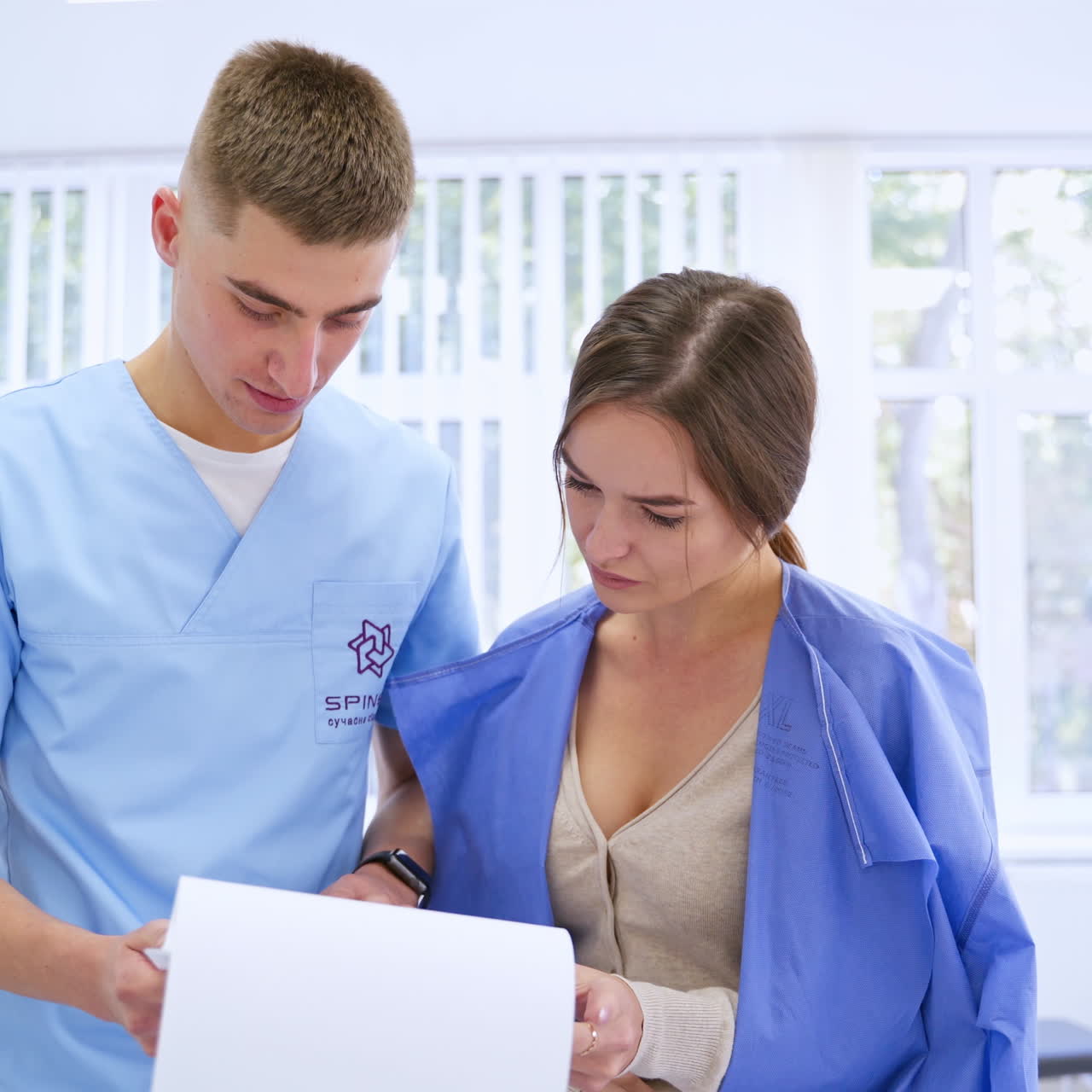 Visitor talking to a doctor about the patient's health. Specialist shows woman the results of patient's check-up in clinic. Senior man laying in a hospital room.