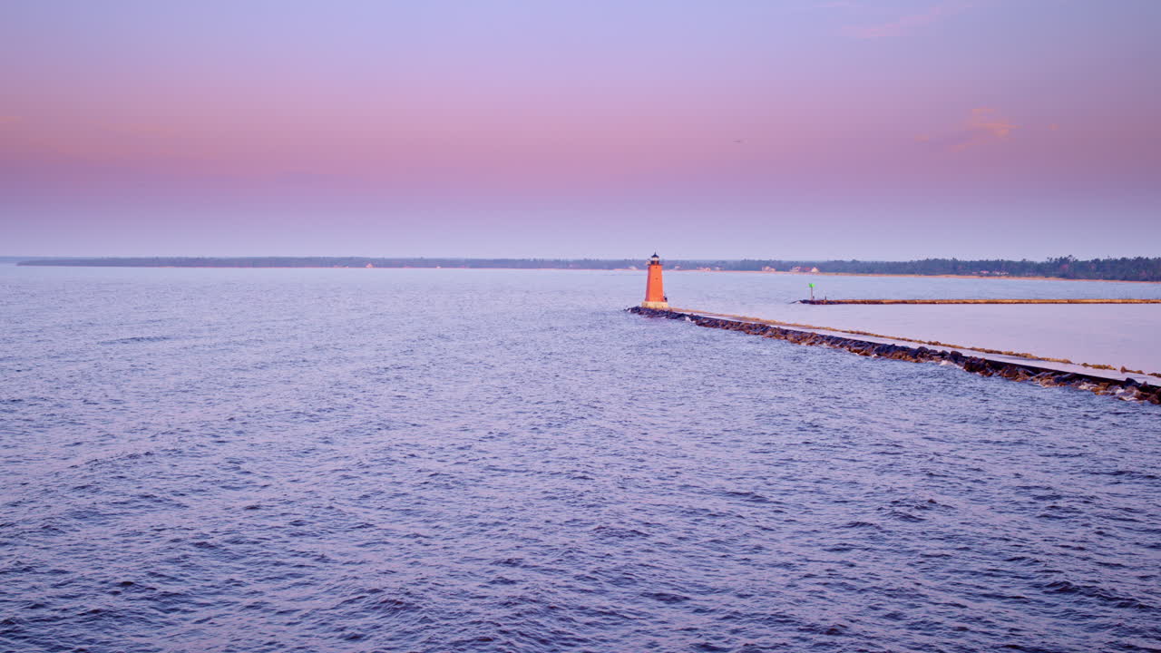 Drone shot flying over lake michigan at sunrise towards a red light house