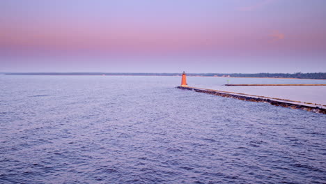 drone shot flying over lake michigan at sunrise towards a red light house