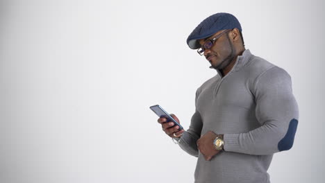 happy young african american man with a phone. black man with a sportive body writing messages on mobile phone isolated on studio. side view. people lifestyle concept.