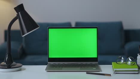 Arbeitsplatz-Am-Wohnzimmertisch-Eines-Freiberuflers-Mit-Laptop,-Lampe,-Buch-Und-Brille,-Greenscreen-Für-Chroma-Key-Technologie,-Zoom-Aufnahme