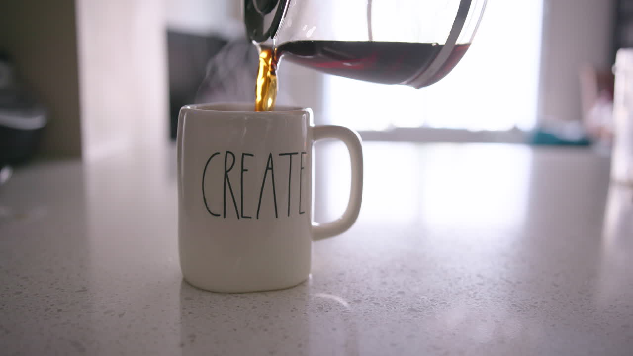 cafetera vertiendo café en una taza con "crear" antes de que una mano saque la taza del marco