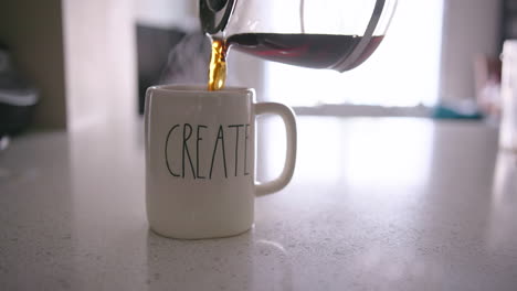 coffee pot pouring coffee into a mug with "create" on it before a hand pulls the mug out of frame