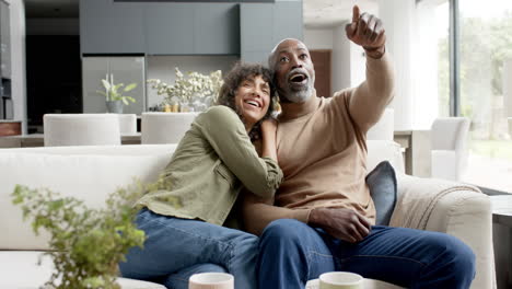 happy biracial couple embracing and watching tv at home, slow motion