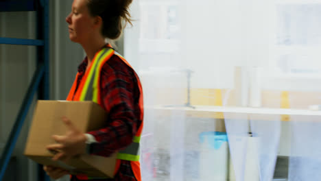 Front-view-of-caucasian-female-worker-walking-with-cardboard-box-in-factory-4k