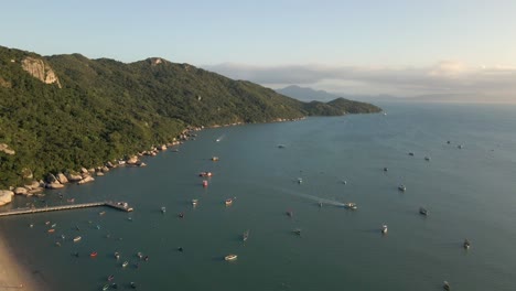 small boats anchored in the sea with green mountain coastline, aerial